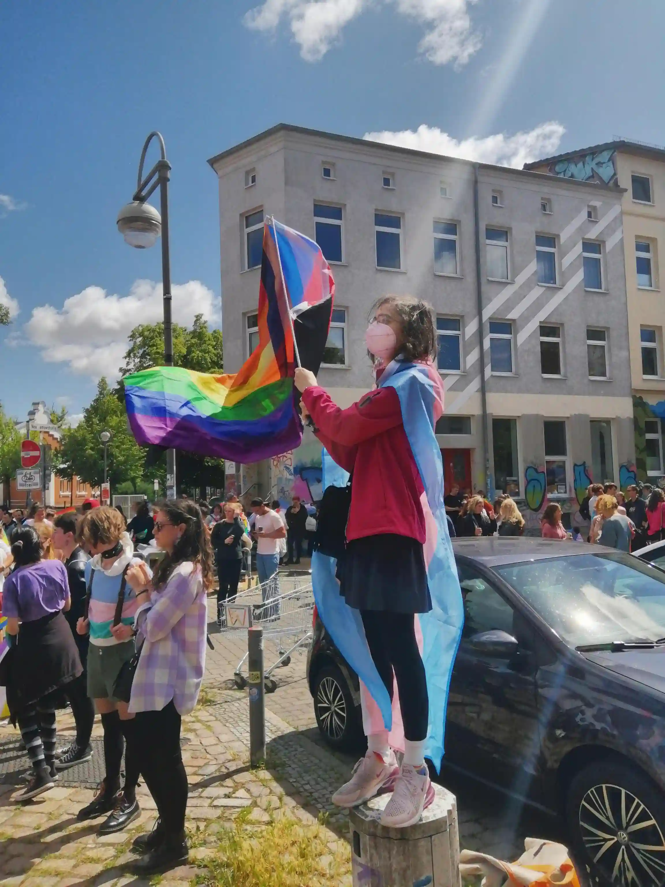 Us, wearing the same outfit, standing on some sort of crate or so, waving our flag, polyamorous flag being better visible this time