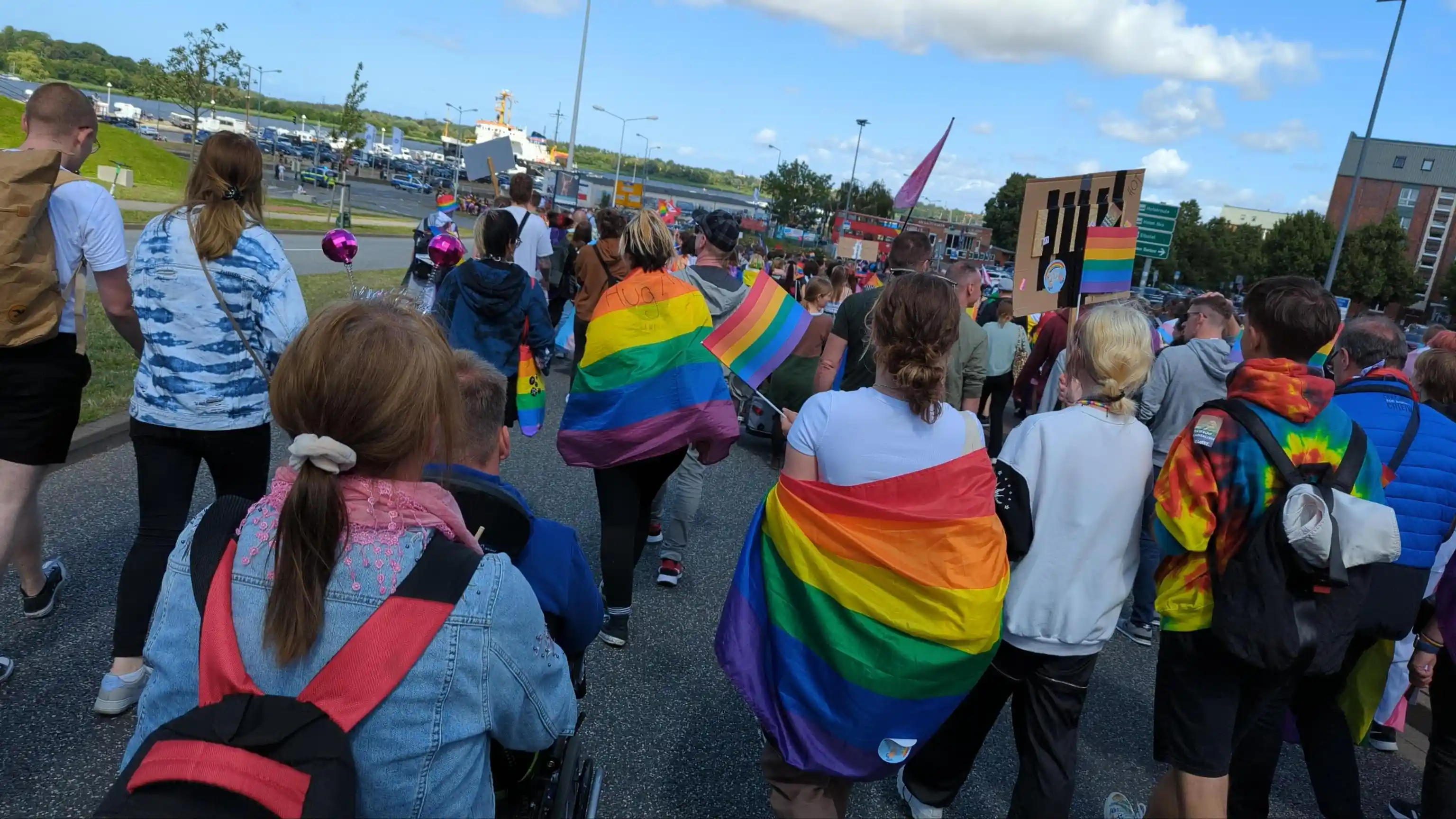 Rainbow people walking towards some body of water, presumably the harbour area