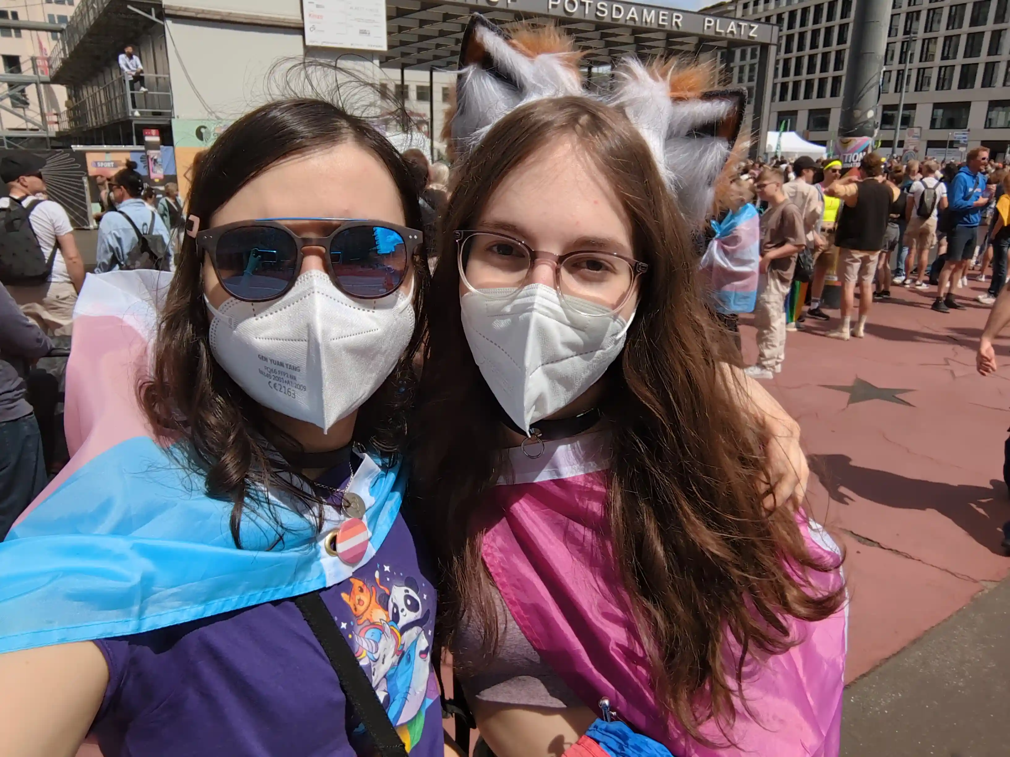 Artemis and Anna, hugging while wearing pride flag capes