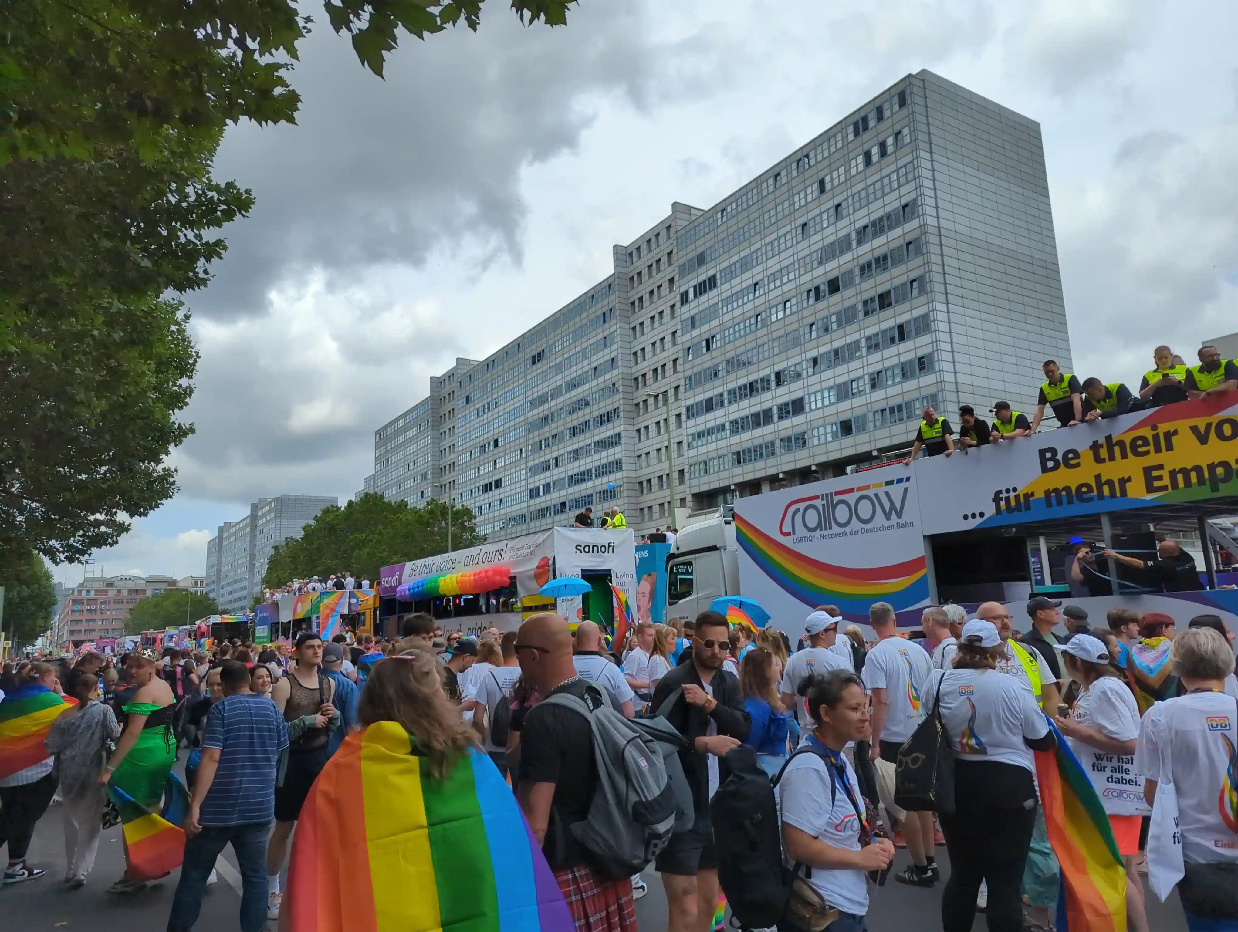 Lots of rainbow people in front of various trucks with ads on them